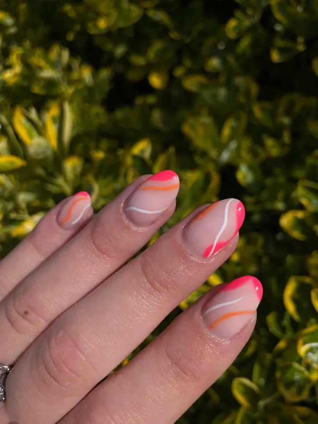 Nagels met dunne roze en oranje lijnen, voor een groene struik.