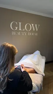 Behandelkamer met de tekst Glow Beauty House op de muur en een klant op het behandelbed.